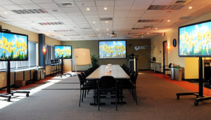 A conference room with a large table and 4 large tv screens with yellow daisies on the screen